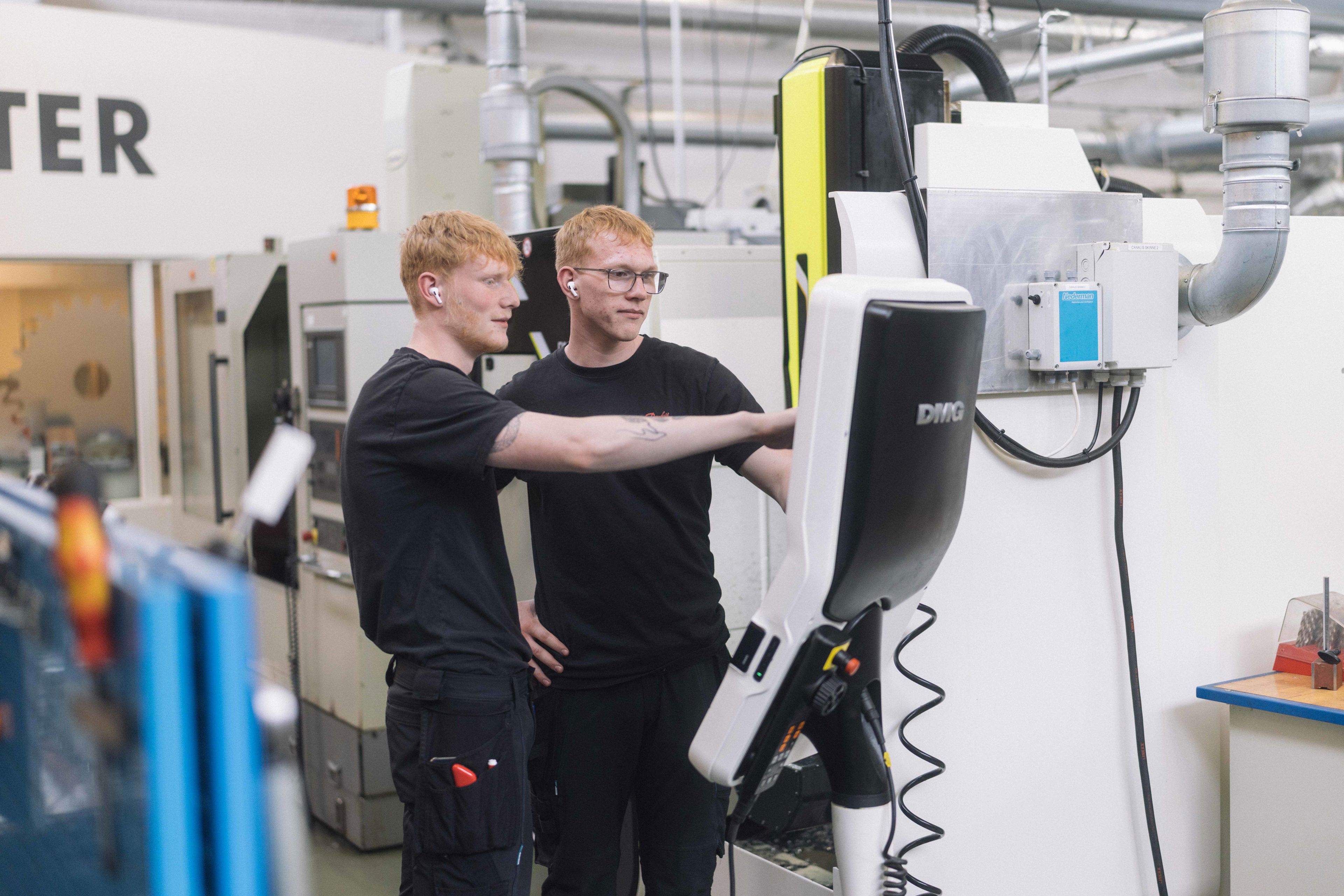 To unge mænd står og kigger på en skærm foran en stor maksine.