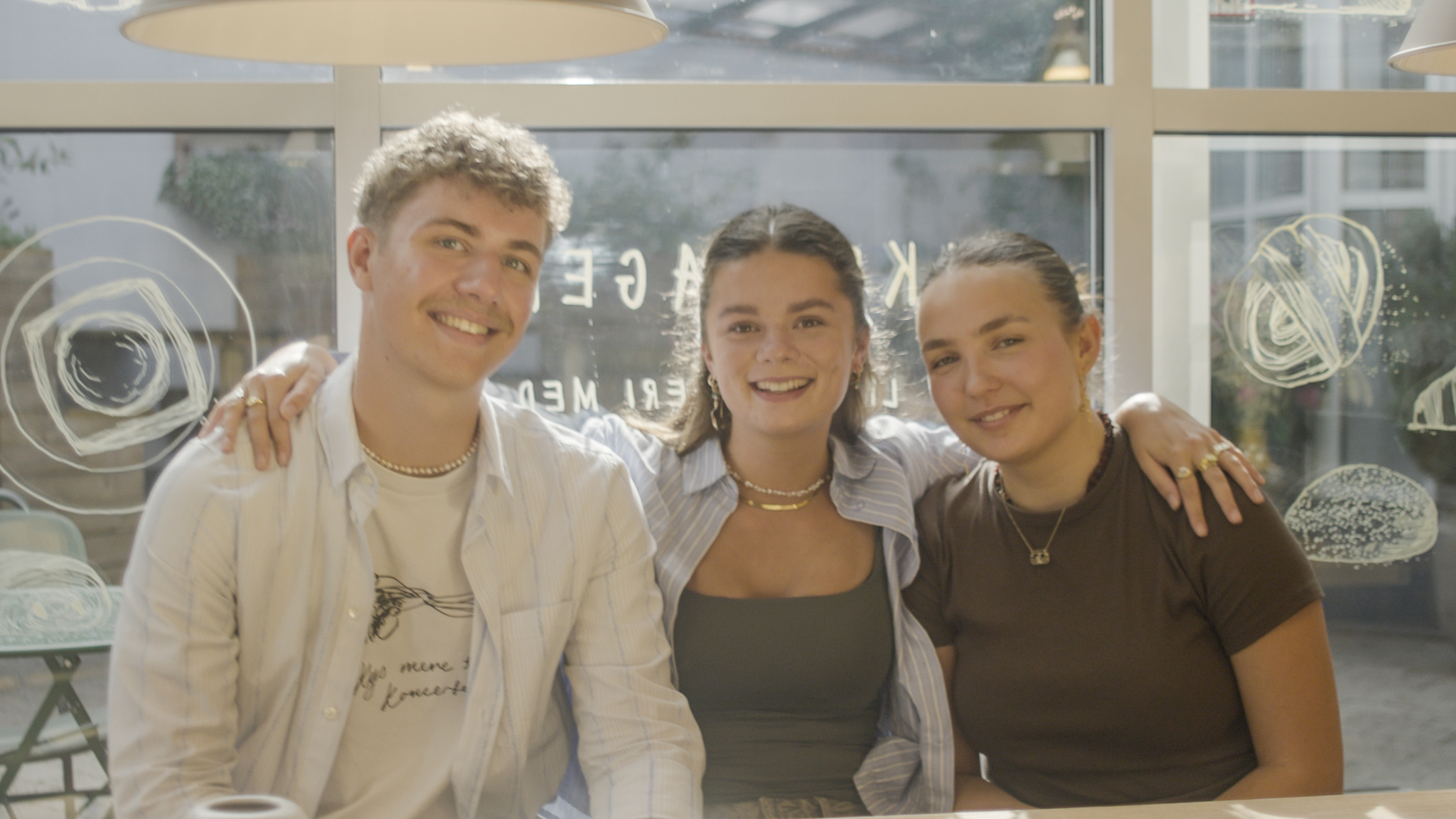 Tre unge studerende sidder sammen og smiler til kameraet.